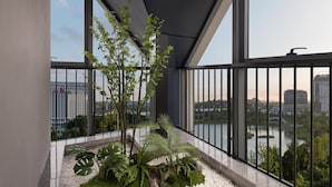 Un balcón con vistas a un lago y edificios, con un arreglo de plantas en macetas y barandilla metálica.