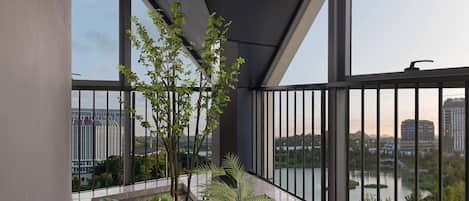 A balcony with a view of a lake and buildings, featuring a potted plant arrangement and a metal railing.