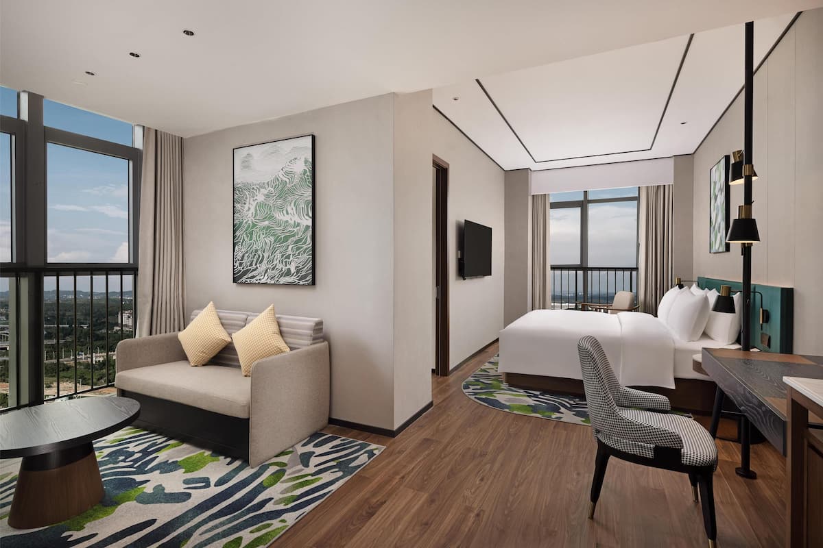 Una moderna camera d'albergo con un letto grande, un divano, un tavolo da pranzo e una sedia. Un'ampia finestra offre vista sulla città.