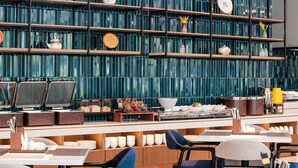 Un restaurante moderno con una barra larga, varias zonas de estar y una pared decorativa con estantes.