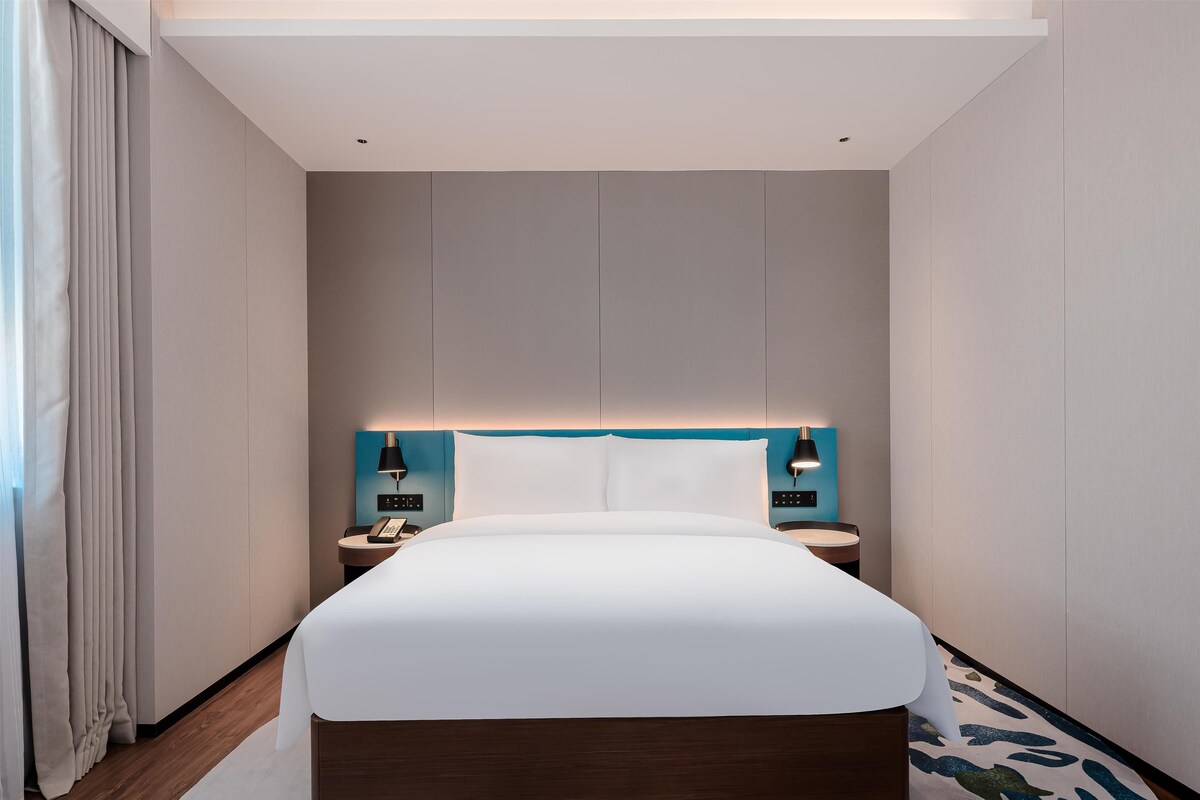 A modern hotel room with a large bed, bedside tables, and a headboard with integrated lighting.