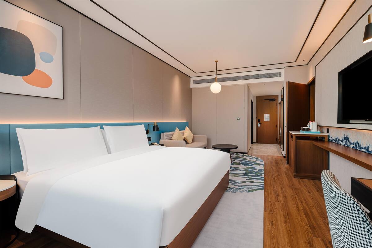 A hotel room with a large bed, a desk, a television, and a sofa.