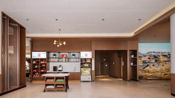 A hotel lobby with a reception desk, vending machines, and a large mural on the wall.
