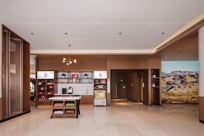 Un vestíbulo de hotel con mostrador de recepción, máquinas expendedoras y un gran mural en la pared.