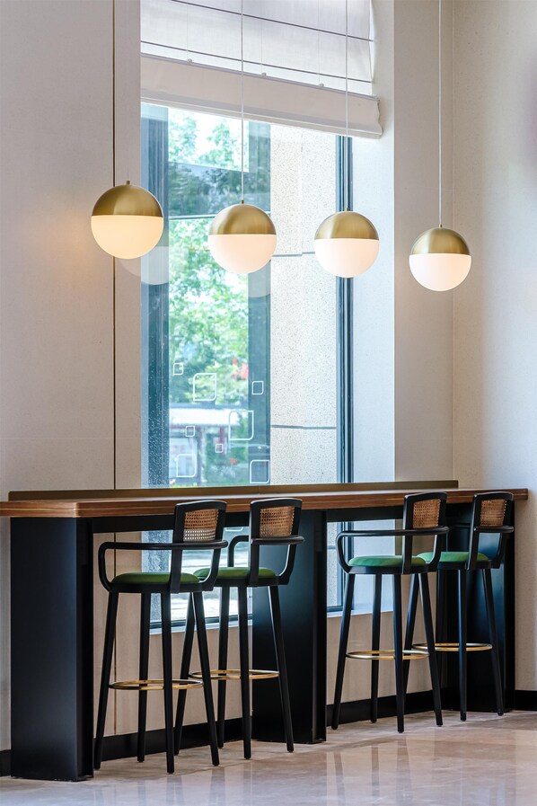 A modern bar area with a long counter, four black chairs with green cushions, and three hanging pendant lights.