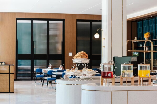 Un vestíbulo moderno de hotel con una mesa redonda central, una zona de estar y una barra con dispensadores de bebidas.