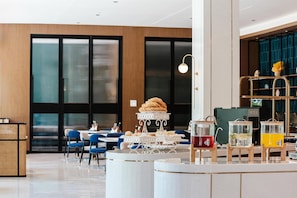 A modern hotel lobby with a central round table, seating area, and a bar area with drink dispensers.