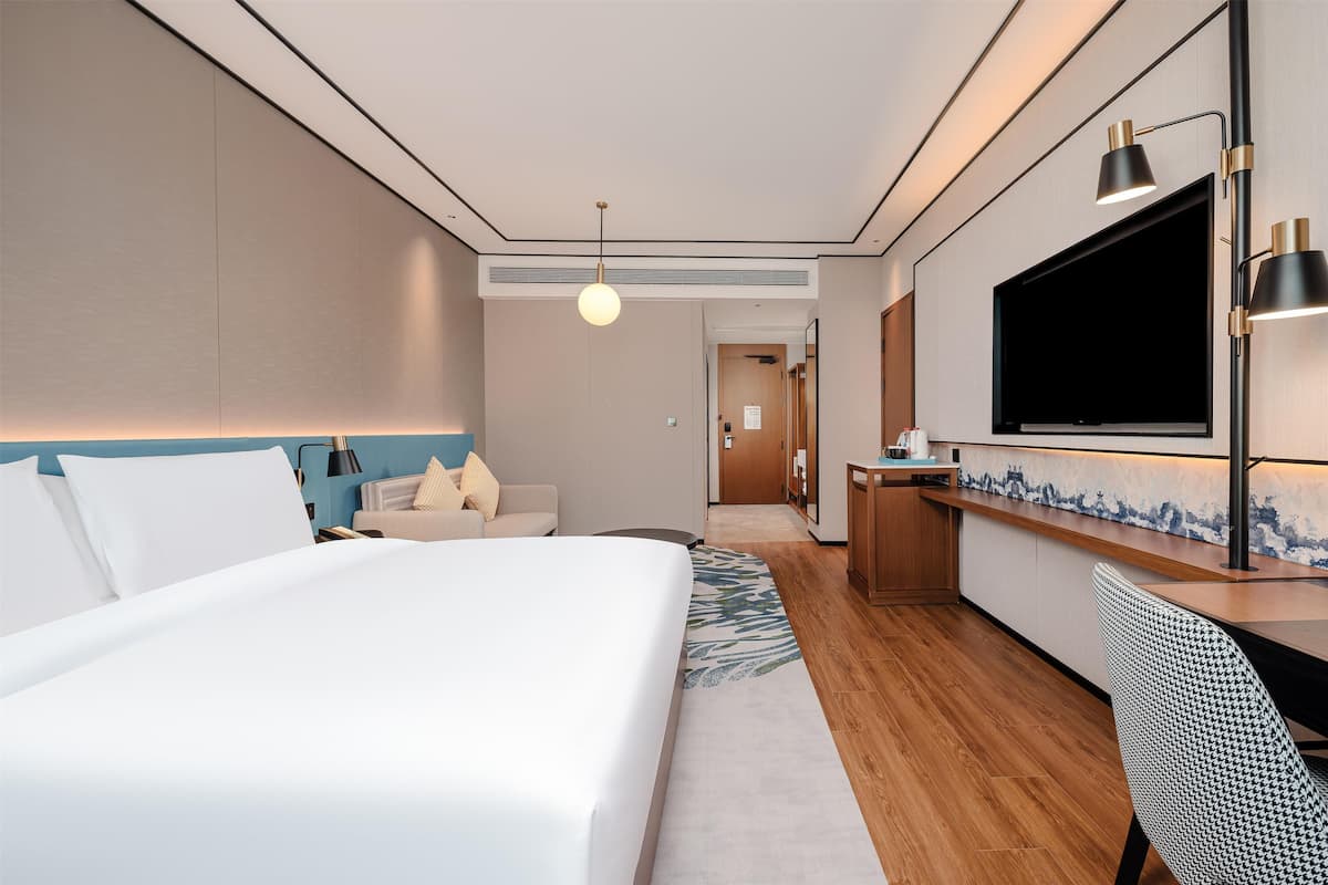 A hotel room with a bed, a desk, a TV, and a bathroom visible in the background.
