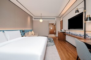 A hotel room with a bed, a desk, a TV, and a bathroom visible in the background.