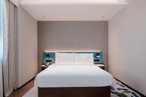 Una habitación de hotel moderna con una cama grande, mesitas de noche y un cabecero con iluminación integrada.