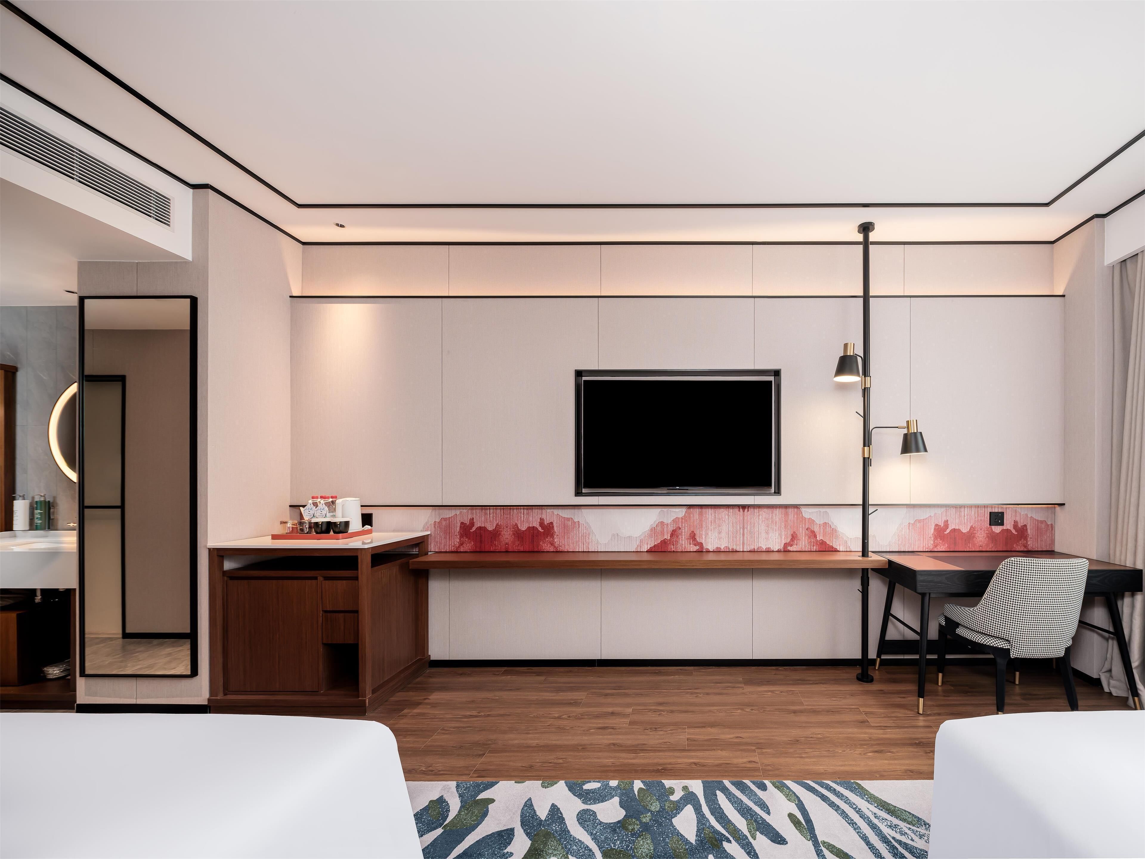 A modern hotel room with a flat-screen TV, a desk, a chair, and a bed.
