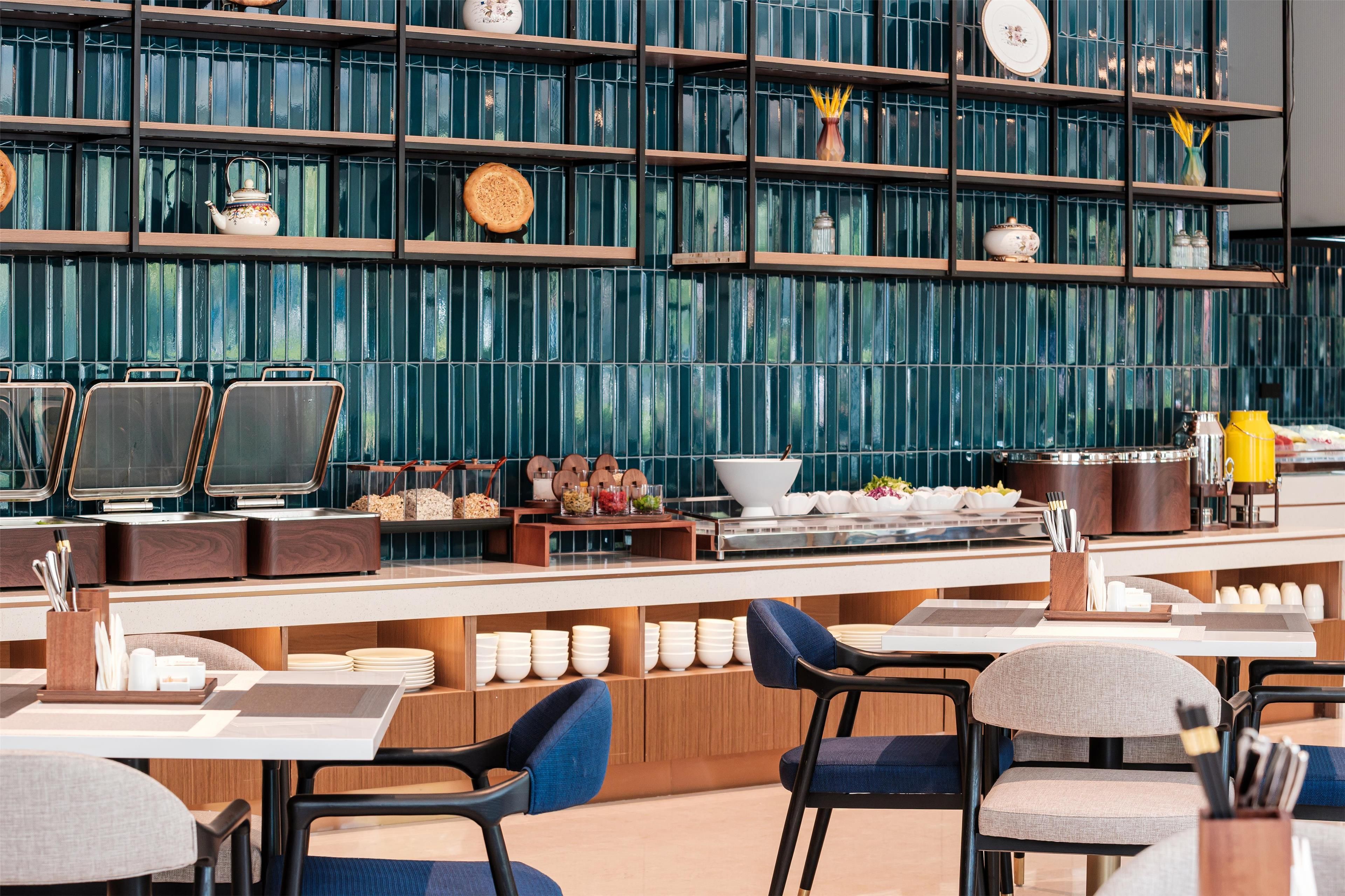 A modern restaurant with a long counter, multiple seating areas, and a decorative wall with shelves.
