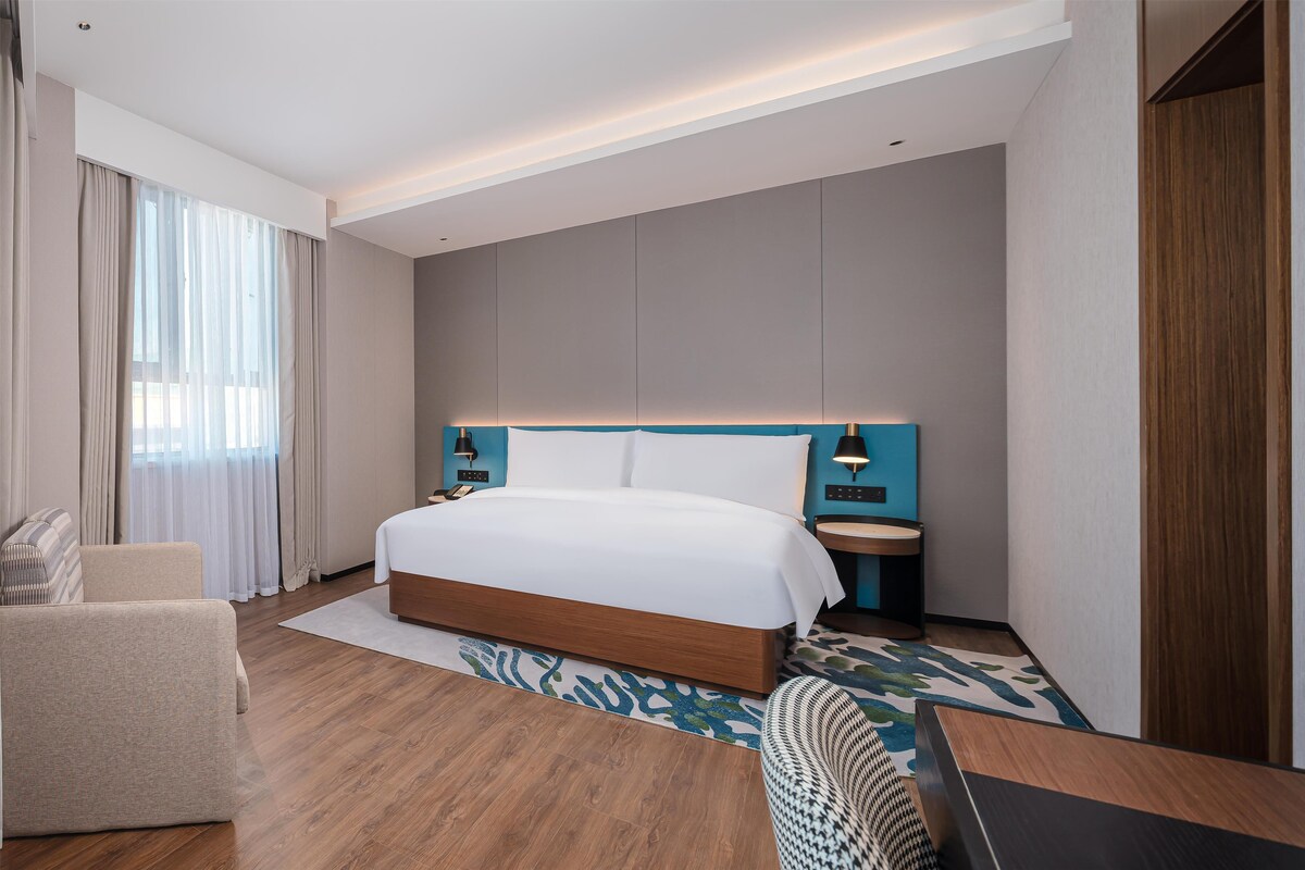 Una habitación de hotel moderna con una cama grande, una mesita de noche, una silla y un escritorio.