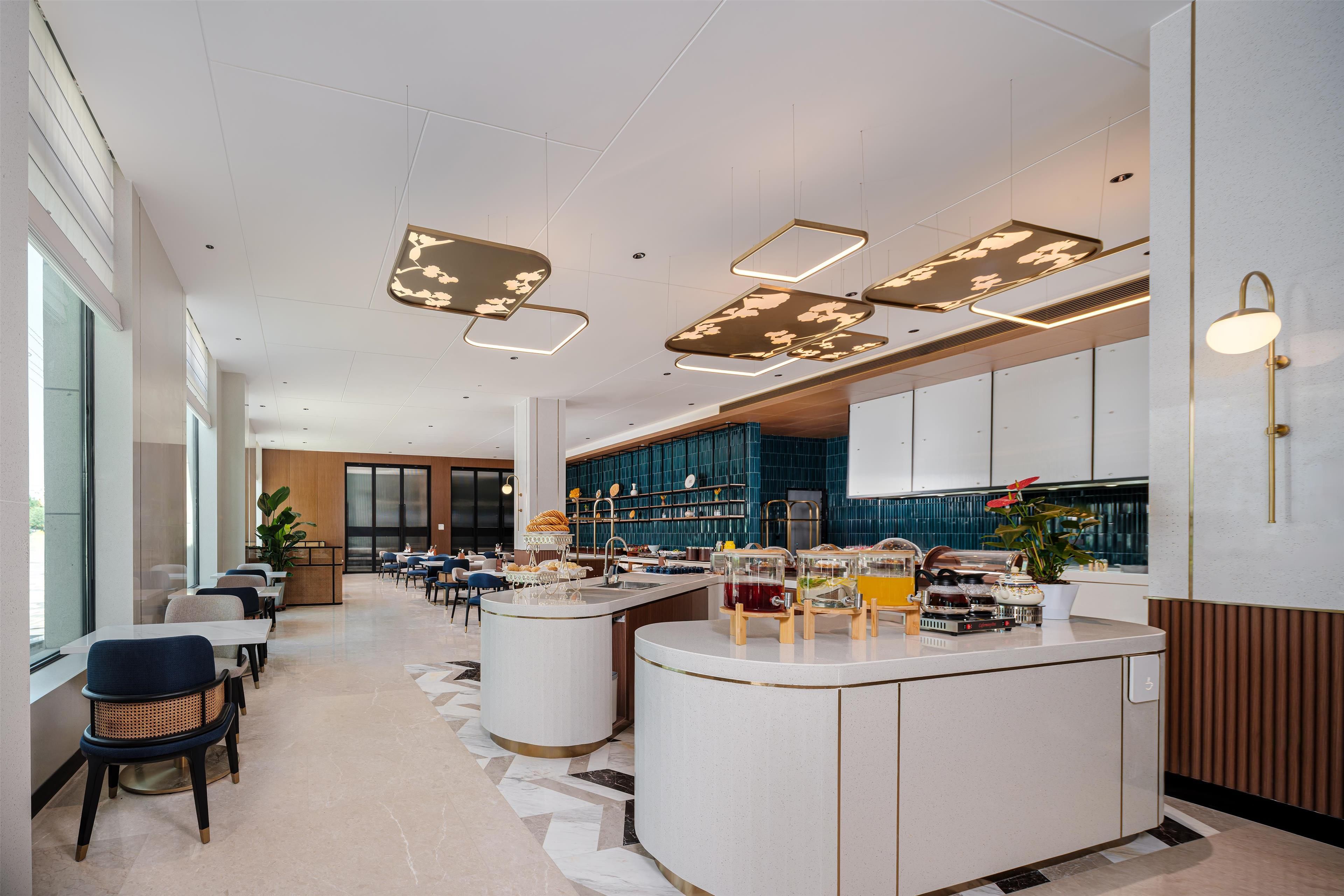 Un hall d’hôtel moderne doté d’un bar central, de différents espaces aménagés pour s’asseoir et d’une grande fenêtre laissant entrer la lumière naturelle.