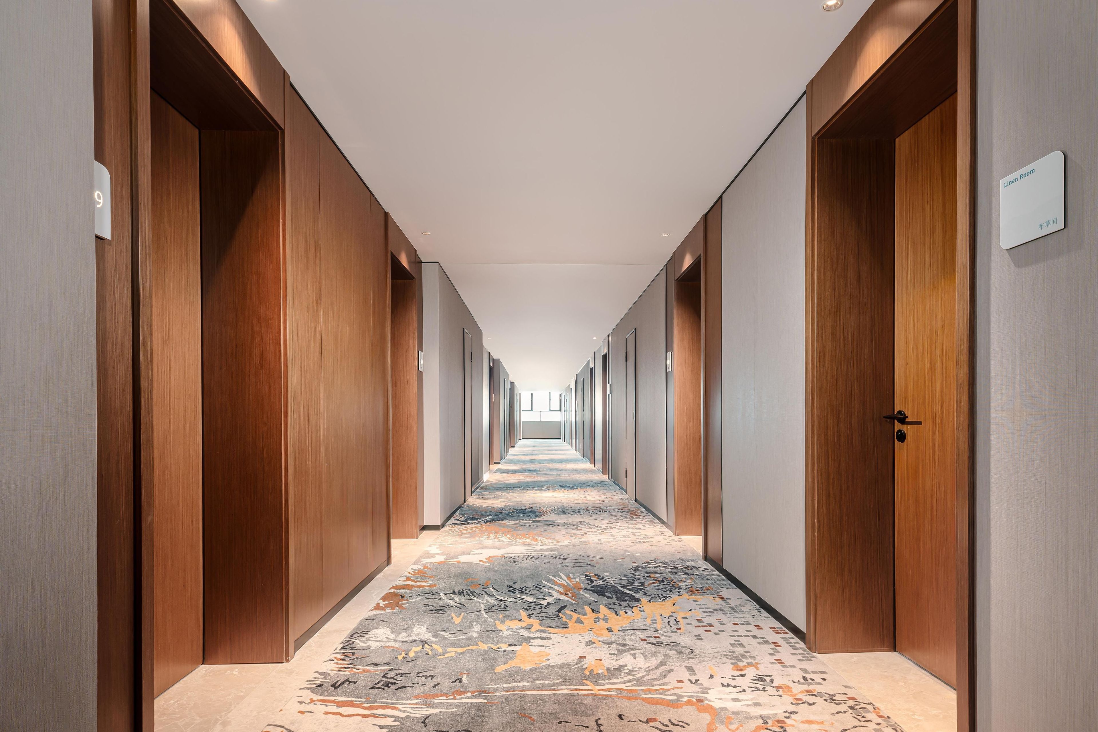 Een hotelgangen met houten deuren, een vloerbedekking en een bordje met een kamer aanduiding.