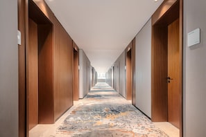 A hotel corridor with wooden doors, a carpeted floor, and a sign indicating a room. - Hilton Garden Inn Yanqi Downtown (Hejing)