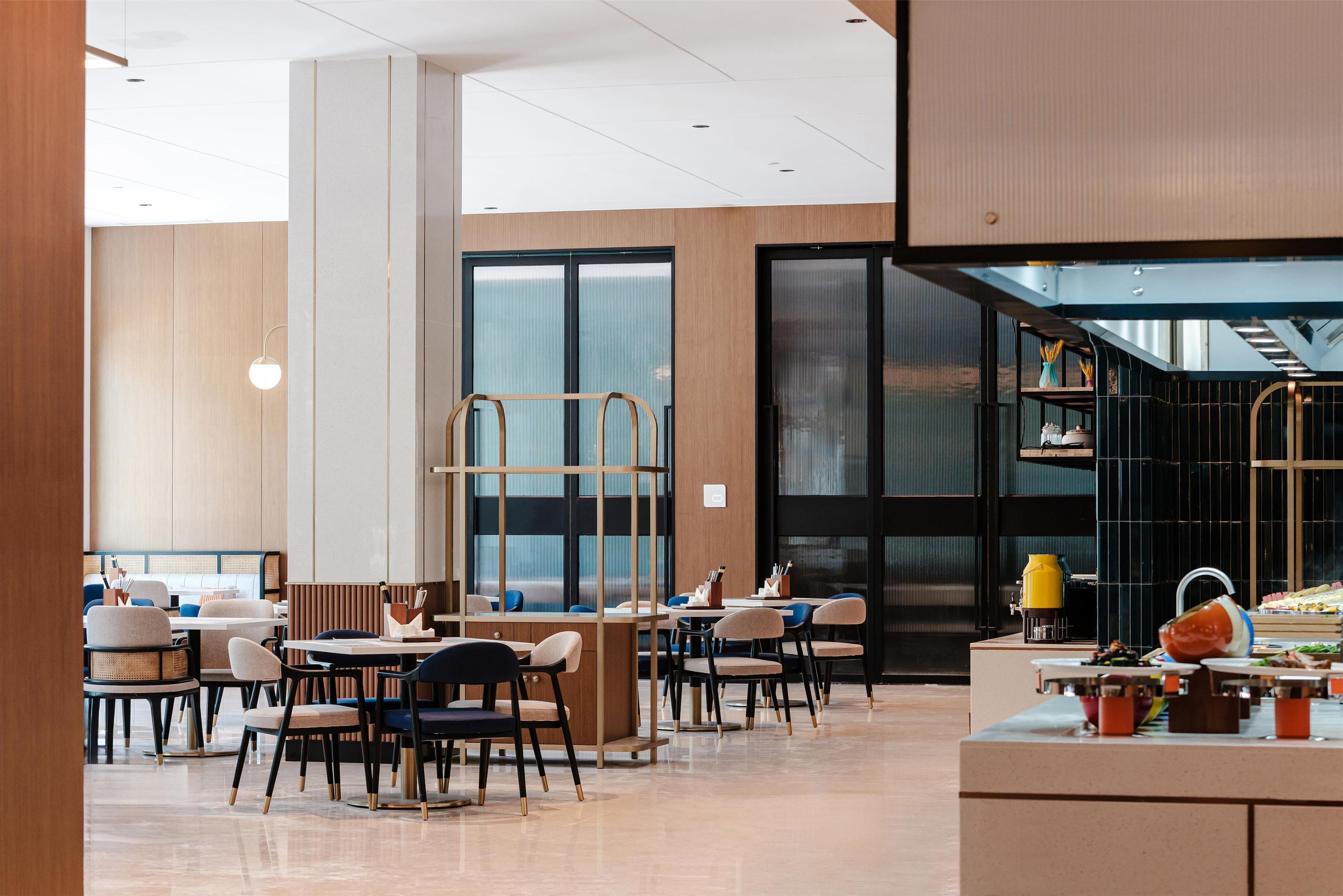 A modern dining area with tables and chairs, a counter with food, and a view of the sky through large windows.