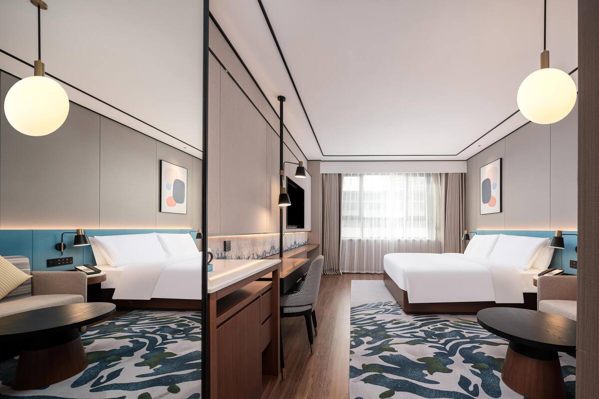 A hotel room with two beds, a desk, a chair, a sofa, and a TV.