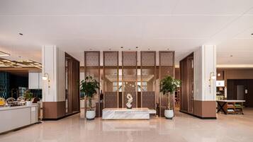 A modern lobby with a reception desk, decorative screens, and potted plants.