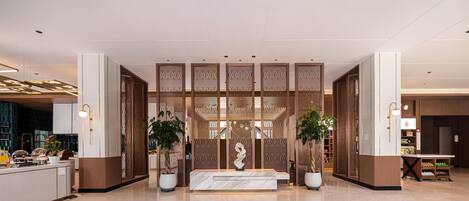 A modern lobby with a reception desk, decorative screens, and potted plants.