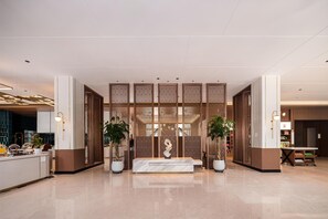 Un vestíbulo moderno con mostrador de recepción, paneles decorativos y plantas en macetas.
