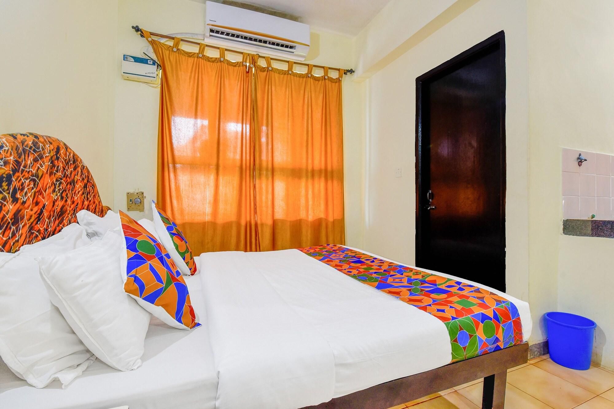 A hotel room with a bed, orange curtains, a black door, and a blue trash bin.