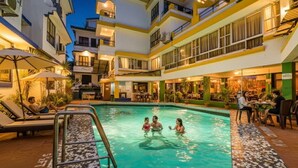 A swimming pool with lounge chairs and a restaurant area in a hotel courtyard. - Fabexpress Alor Holiday Resort (Calangute)