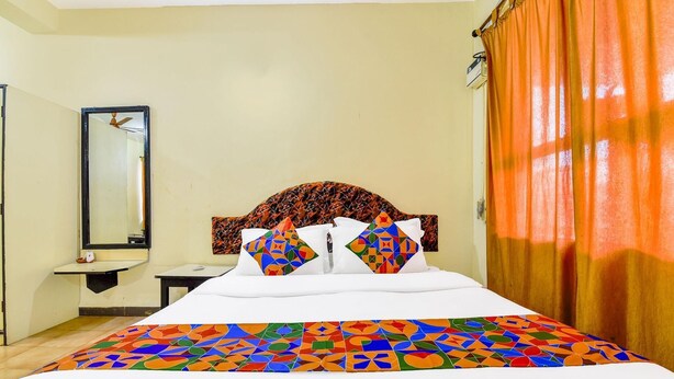 A hotel room with a bed, a nightstand, a mirror, and a window with curtains. - Fabexpress Alor Holiday Resort (Calangute)