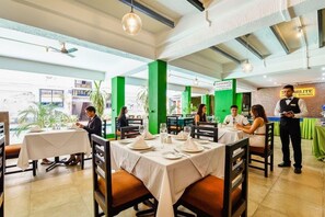 A restaurant with tables set for dining, a waiter attending to guests, and a sign indicating the restaurant name. - Fabexpress Alor Holiday Resort (Calangute)