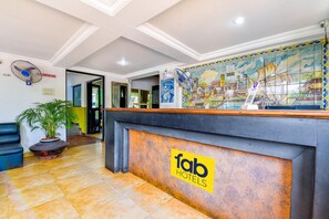 A hotel reception area with a tiled floor, a reception desk with a 'fab hotels' logo, a large mural of a coastal scene, and a 'no smoking' sign. - Fabexpress Alor Holiday Resort (Calangute)