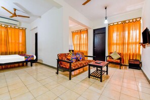 A room with a bed, sofa, and armchair, with orange curtains and a ceiling fan. - Fabexpress Alor Holiday Resort (Calangute)
