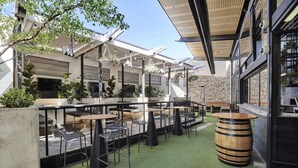 An outdoor seating area with tables and chairs, a wooden barrel, and a stone wall. - Blue Gums Hotel (Adelaide)