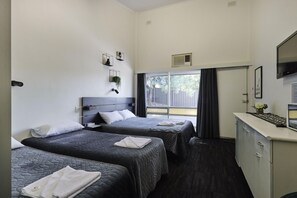 A hotel room with two beds, a TV, a desk with a mirror, and a window with a view of the outside. - Blue Gums Hotel (Adelaide)