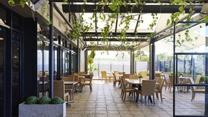 An outdoor patio with wicker furniture and potted plants, featuring a glass enclosure and a view of the surrounding area. - Blue Gums Hotel (Adelaide)