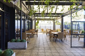 An outdoor patio with wicker furniture and potted plants, featuring a glass enclosure and a view of the surrounding area. - Blue Gums Hotel (Adelaide)