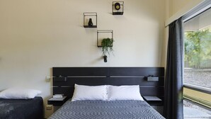 A modern hotel room with a large bed, a bedside table, a small bedside table, a wall-mounted plant, and a window with curtains. - Blue Gums Hotel (Adelaide)