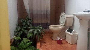 A bathroom with a toilet, sink, shower curtain, and potted plants. - Hotel Cortez (San José)