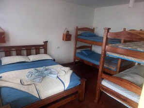 A room with a wooden bunk bed, a single bed, and a small table with a lamp. - Hotel Cortez (San José)