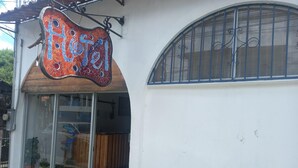 A hotel entrance with a mosaic sign, glass doors, and a wooden interior visible through the doors. - Hotel Cortez (San José)