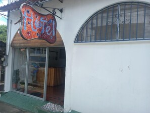A hotel entrance with a mosaic sign, glass doors, and a wooden interior visible through the doors. - Hotel Cortez (San José)