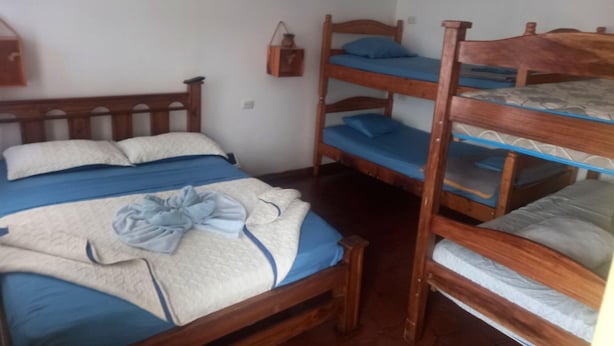 A room with a wooden bunk bed, a single bed, and a small table with a lamp. - Hotel Cortez (San José)