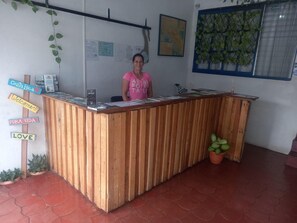 Un mostrador de recepción con detalles de madera, una mujer detrás y varios carteles con las frases 'Costa Rica', 'Bienvenida', 'Pura Vida' y 'Amor'.