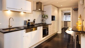 A modern kitchen with white cabinets, a black countertop, stainless steel appliances, and a bar area with stools. - The Notting Hill Gate Crib Relaxing 2bdr House (London)