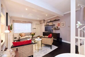 Ein modernes Wohnzimmer mit Sofa, zwei Sesseln, Couchtisch, Fernseher und Treppe.