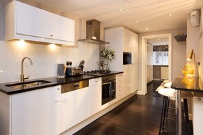 Una cocina moderna con armarios blancos, encimera negra, electrodomésticos de acero inoxidable y una zona de bar con taburetes.