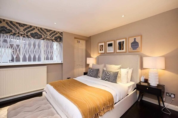 A bedroom with a bed, bedside tables, a window with a patterned curtain, and wall-mounted artwork. - The Notting Hill Gate Crib Relaxing 2bdr House (London)