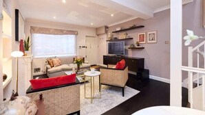 A modern living room with a sofa, two chairs, a coffee table, a TV, and a staircase. - The Notting Hill Gate Crib Relaxing 2bdr House (London)