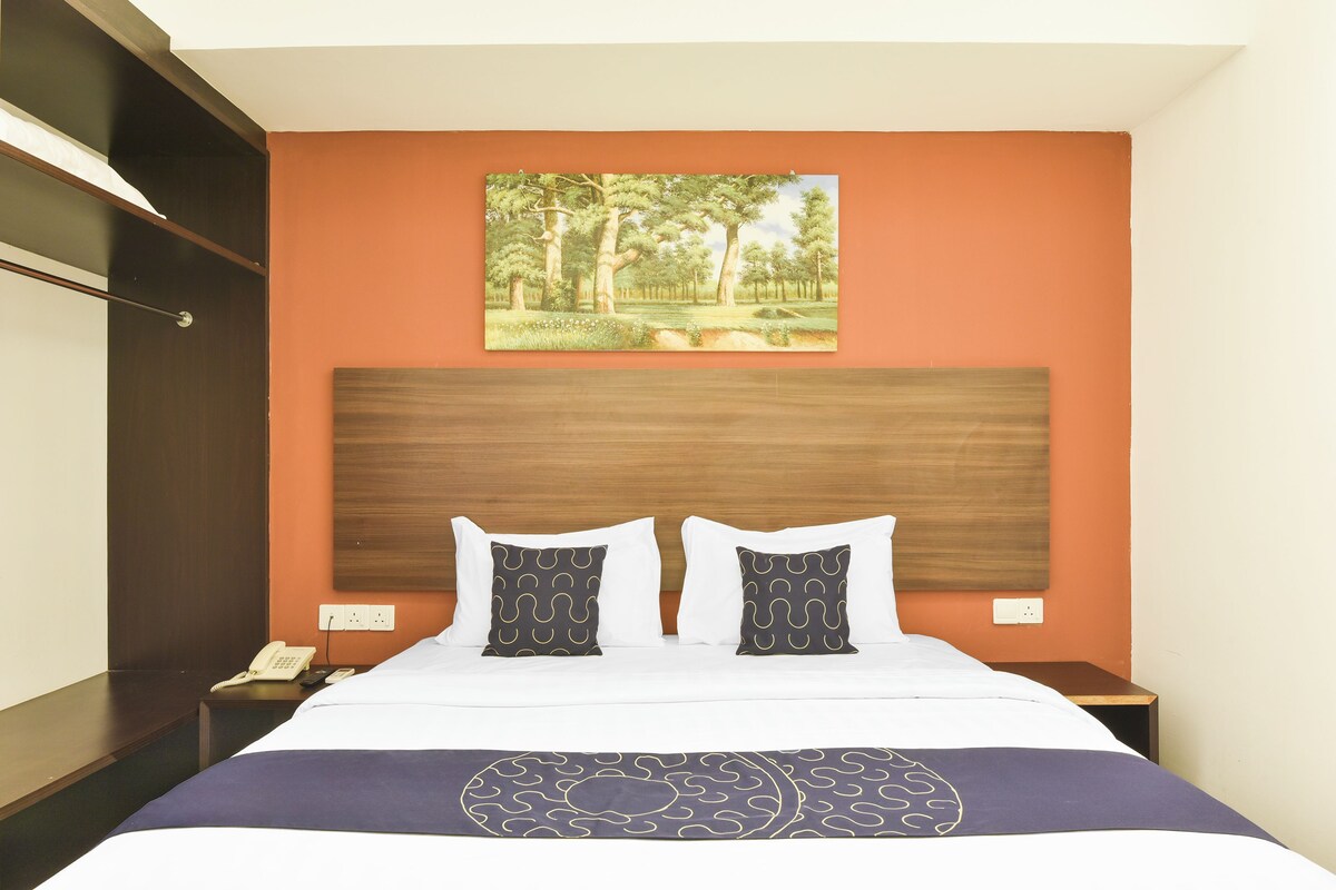 A hotel room with a bed, two bedside tables, a painting of a forest, and a wooden headboard.