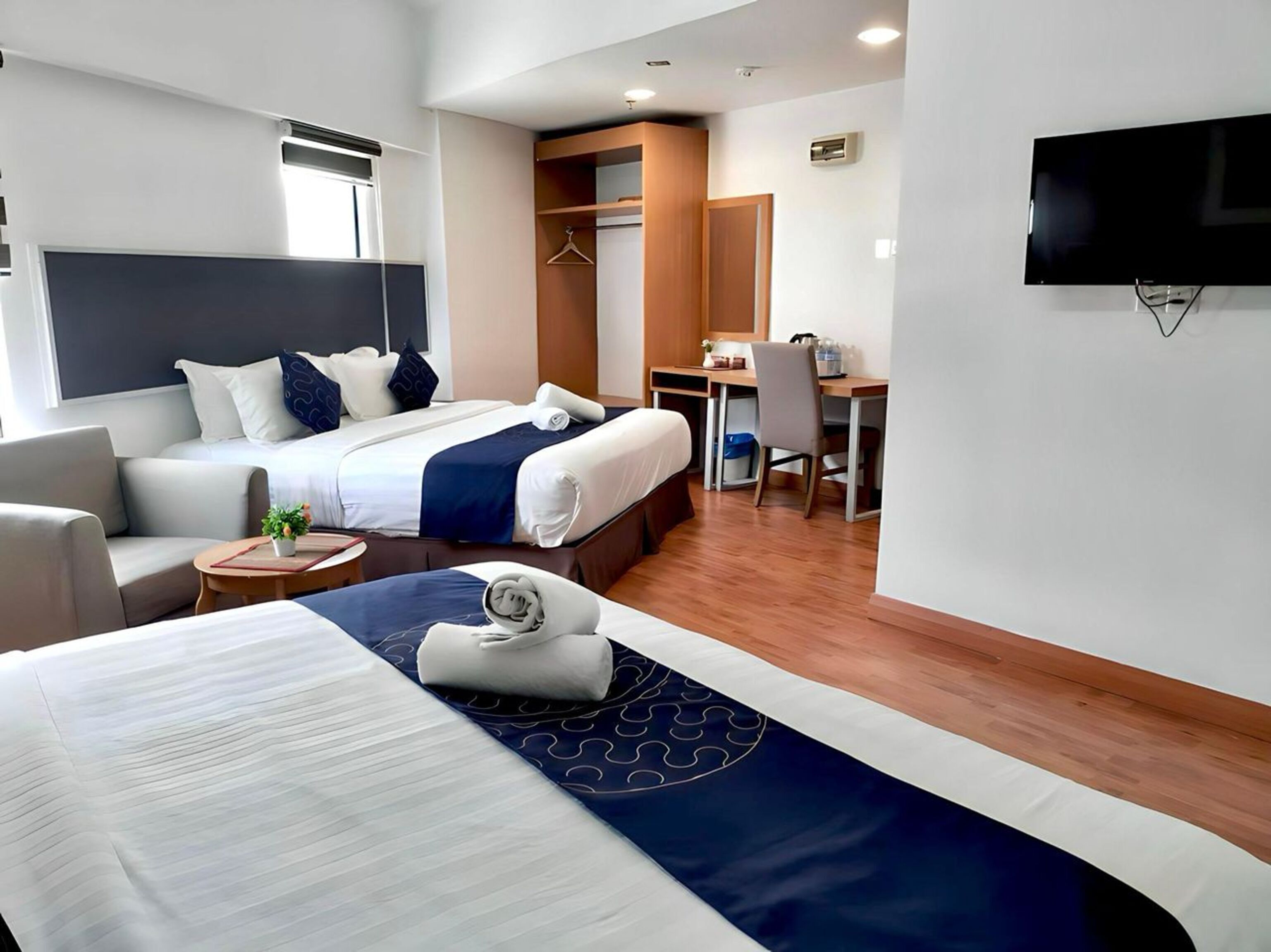 Une chambre d’hôtel avec deux lits, un bureau, une chaise, une télévision et une petite table avec une plante.