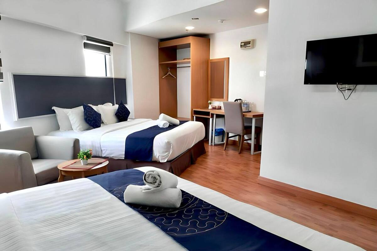 Hotelkamer met twee bedden, een bureau, een stoel, een televisie en een klein tafeltje met een plant.